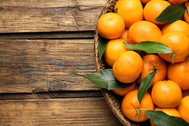 Photo of Fresh ripe tangerines with leaves and space for text on wooden table, top view. Citrus fruit