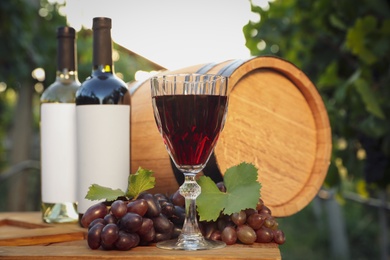 Composition with wine and ripe grapes on wooden table in vineyard