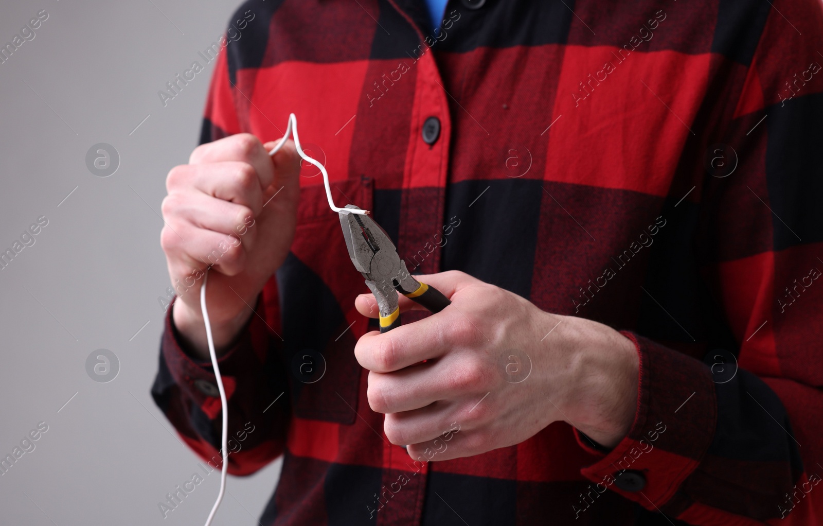 Photo of Young man holding pliers and wire on grey background, closeup