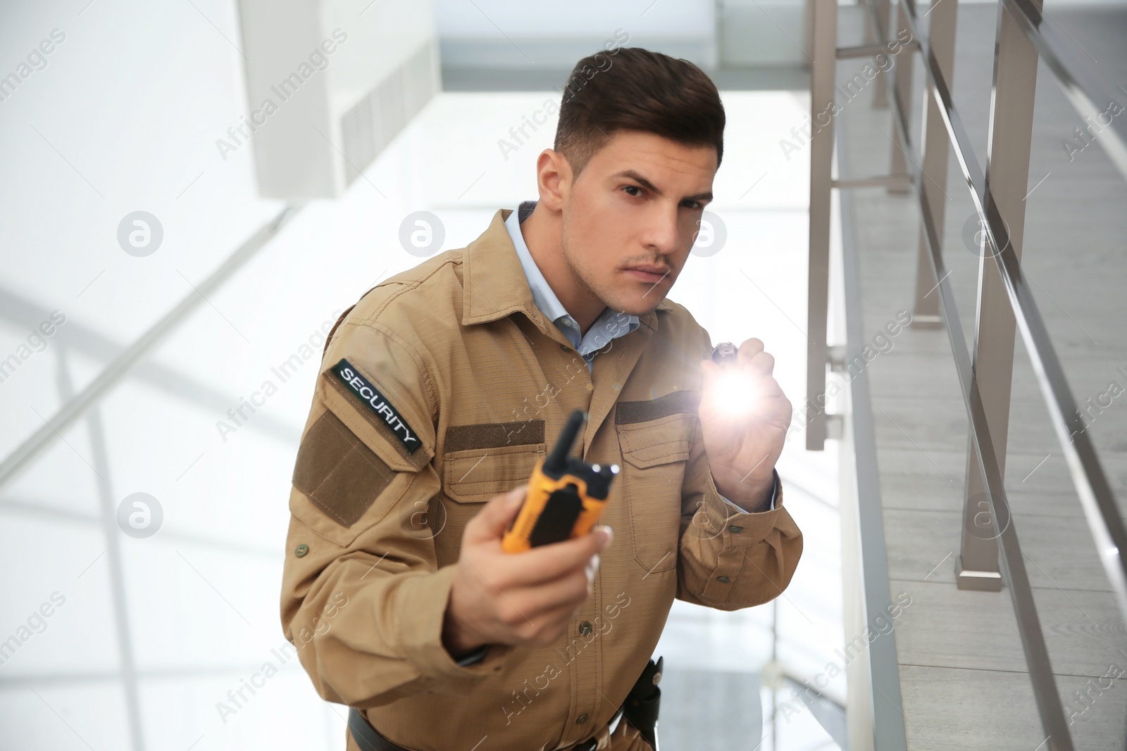 Photo of Professional security guard with portable radio set and flashlight on stairs