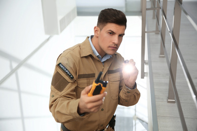 Professional security guard with portable radio set and flashlight on stairs