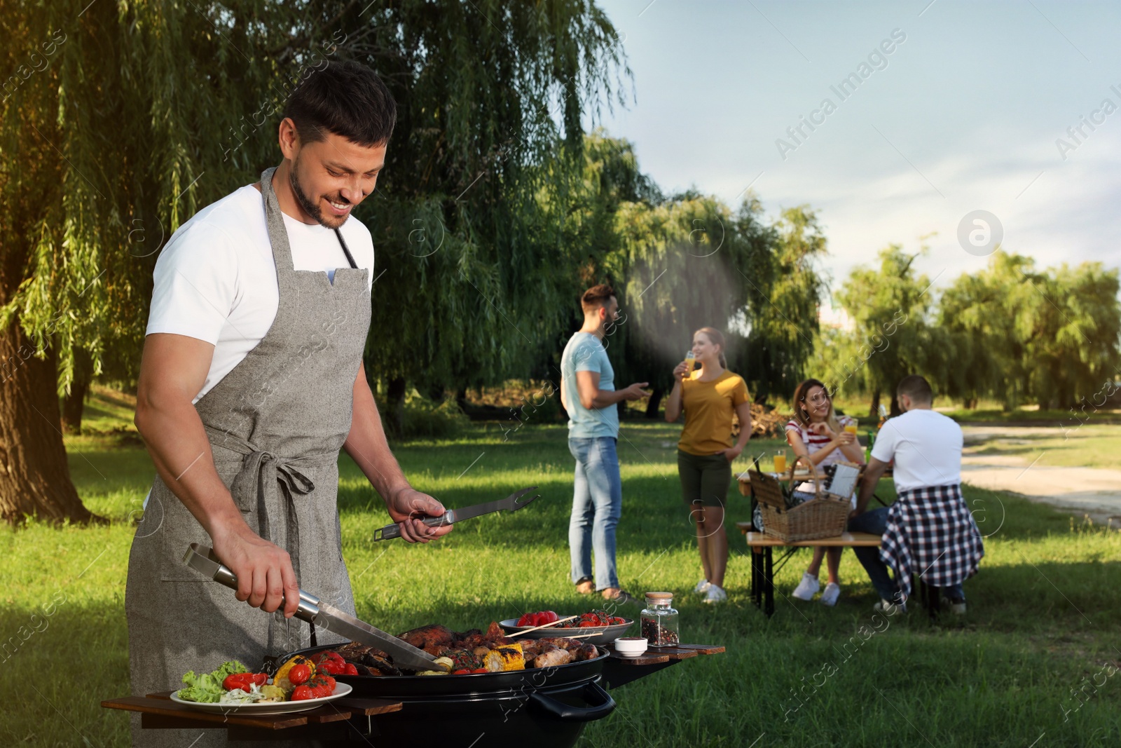 Photo of Man cooking meat and vegetables on barbecue grill in park