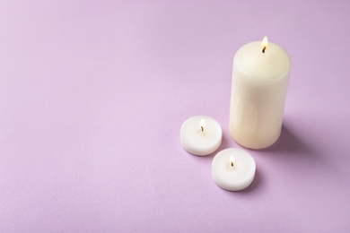 Photo of Burning wax candles of different shapes on color background