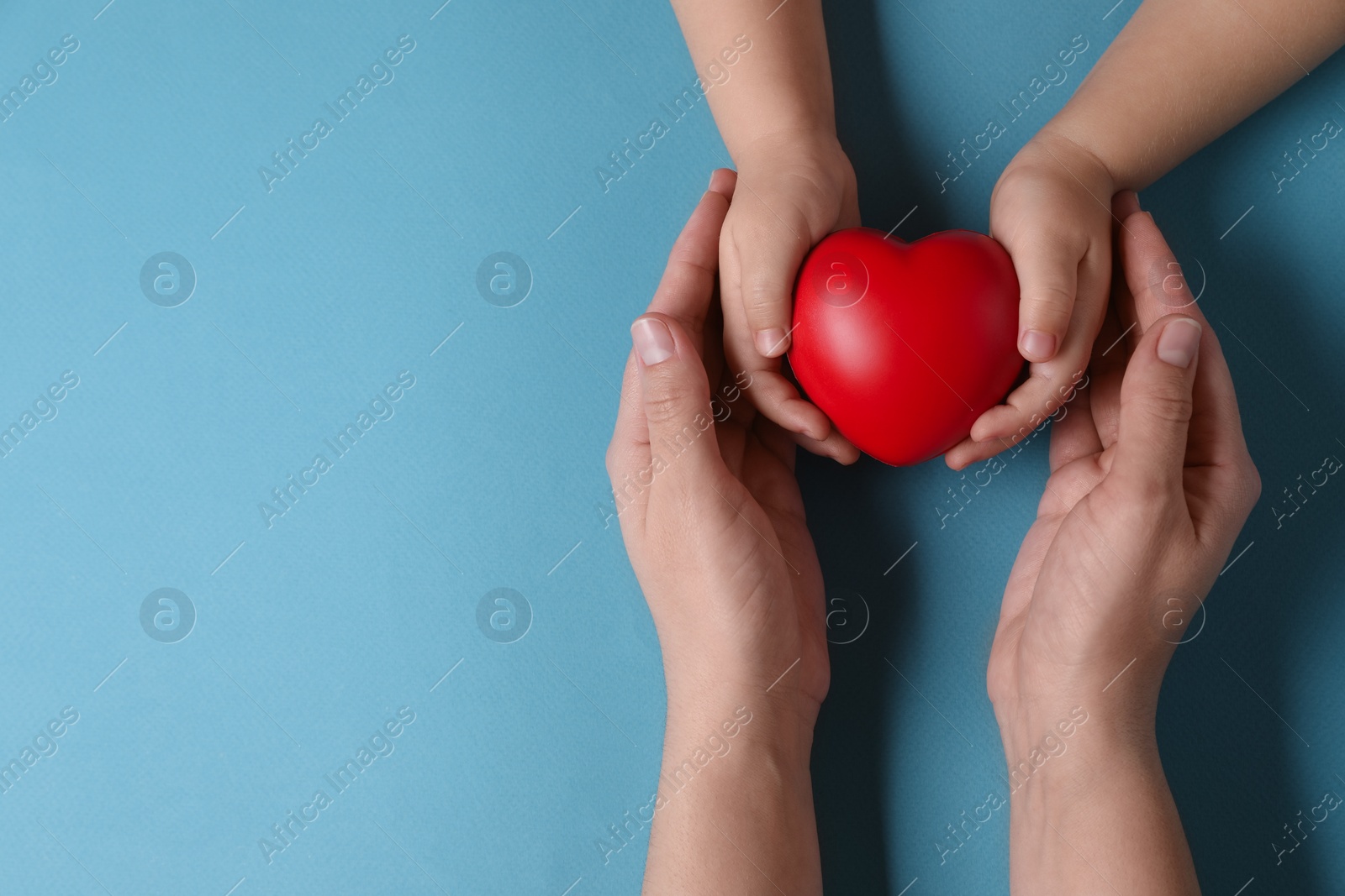 Photo of Mother and her child holding red decorative heart on light blue background, top view. Space for text