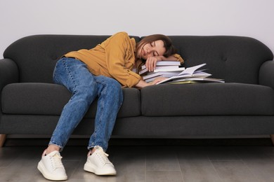 Photo of Young tired woman sleeping near books on couch indoors