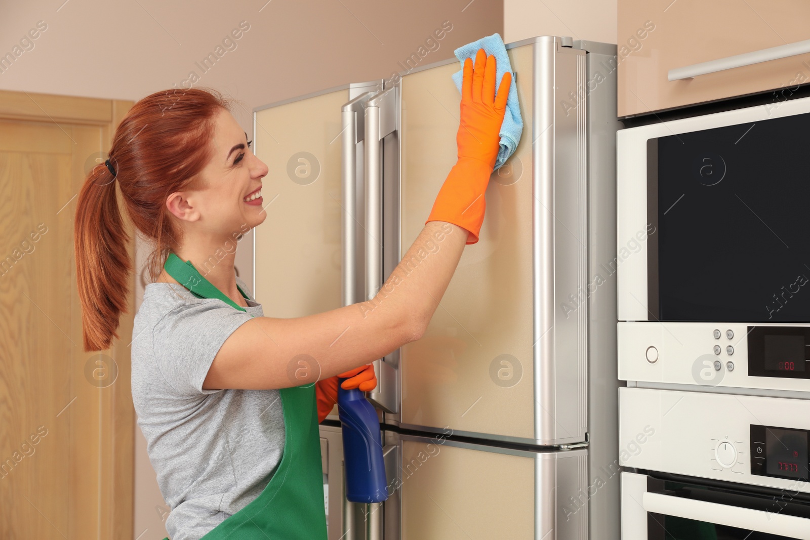 Photo of Woman in protective gloves cleaning refrigerator with rag indoors