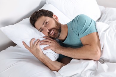 Happy man lying on comfortable pillow in bed at home