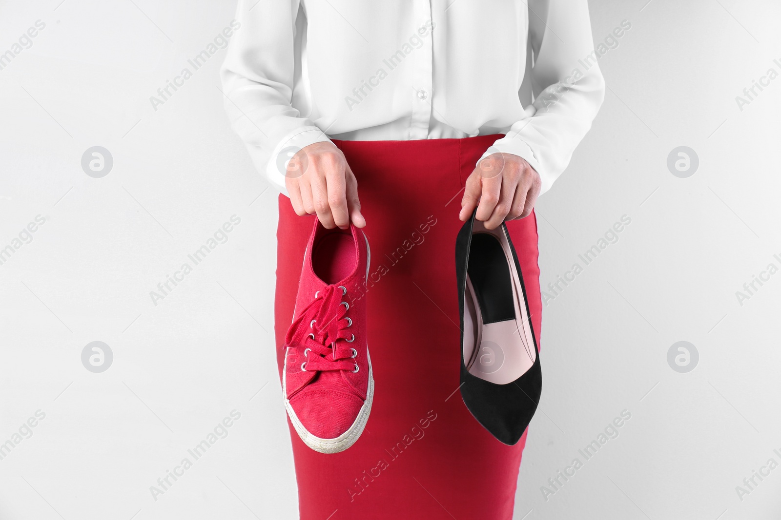 Photo of Woman holding high heeled shoe and sneaker on white background, closeup. Choice concept