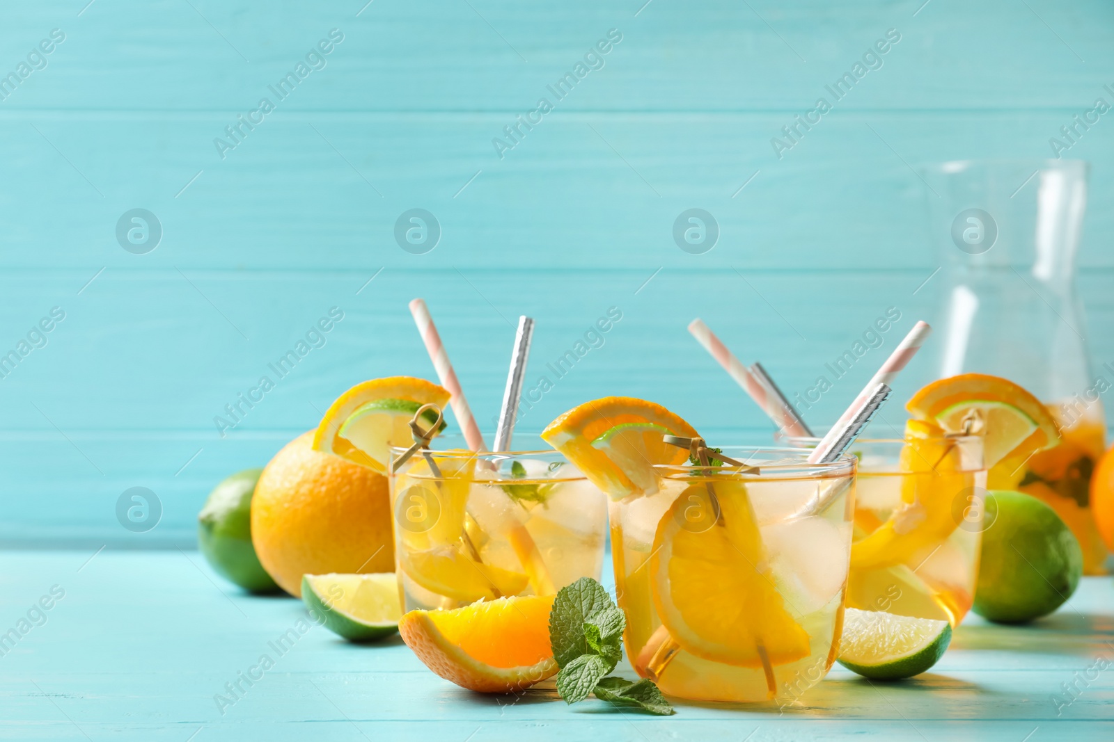 Photo of Delicious refreshing drink with orange and lime slices on light blue wooden table