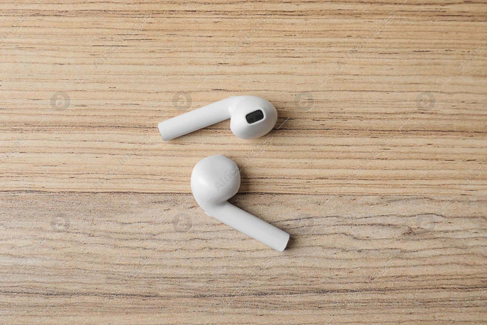 Photo of Pair of modern wireless earphones on wooden table, flat lay