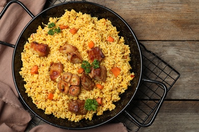 Photo of Frying pan with delicious rice pilaf on wooden background, top view