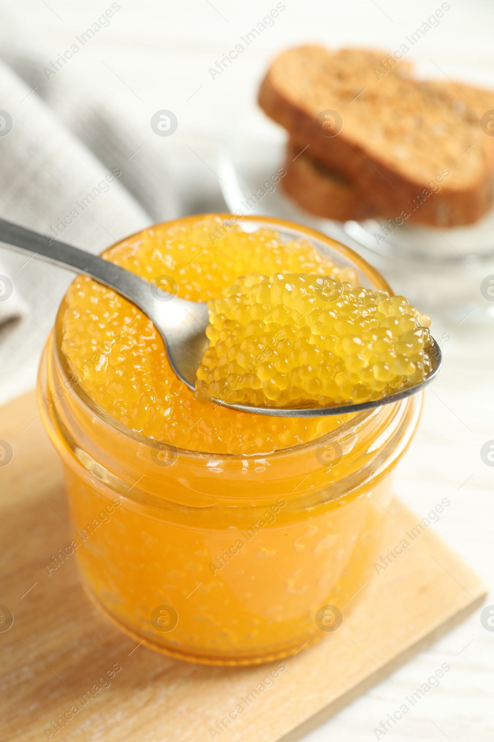 Photo of Taking fresh pike caviar from glass jar on white wooden table, closeup