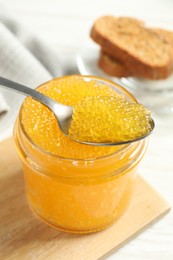 Photo of Taking fresh pike caviar from glass jar on white wooden table, closeup