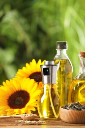 Photo of Many different bottles with cooking oil, sunflower seeds and flowers on wooden table against blurred background