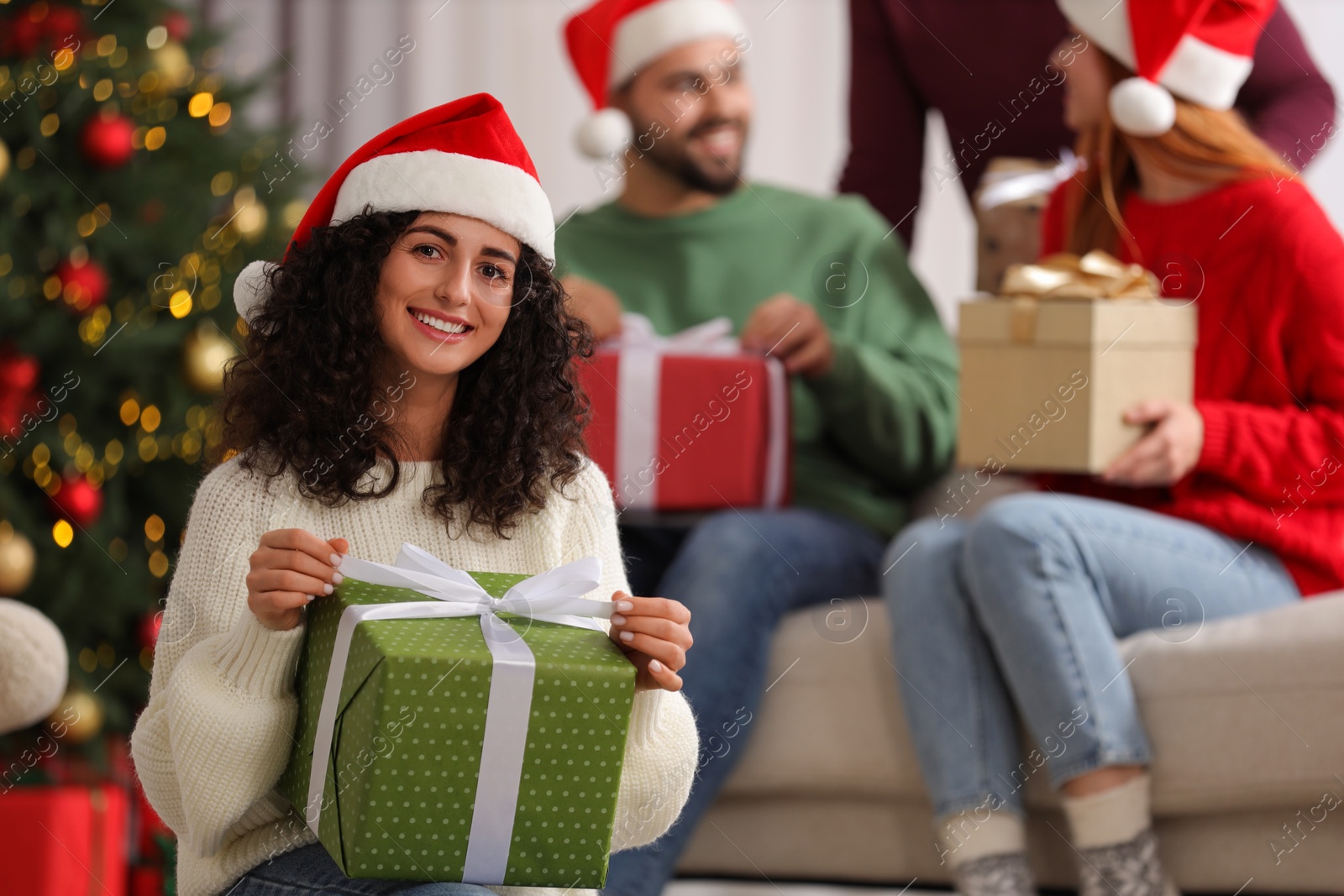 Photo of Christmas celebration in circle of friends. Happy young woman opening gift at home, selective focus