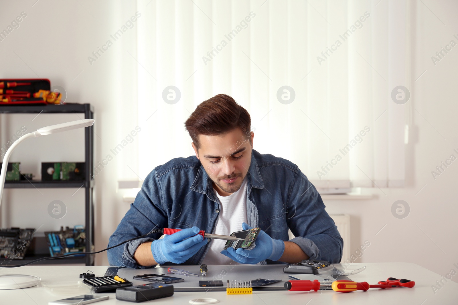 Photo of Technician repairing broken smartphone at table in workshop