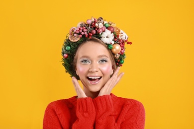 Photo of Beautiful emotional young woman wearing Christmas wreath on yellow background