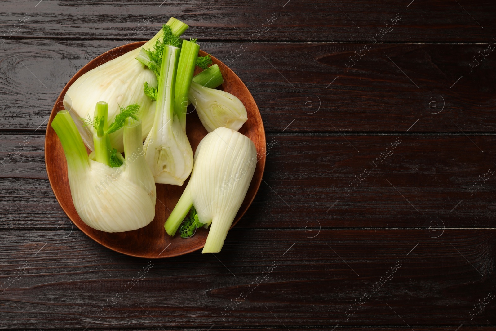 Photo of Whole and cut fennel bulbs on wooden table, top view. Space for text