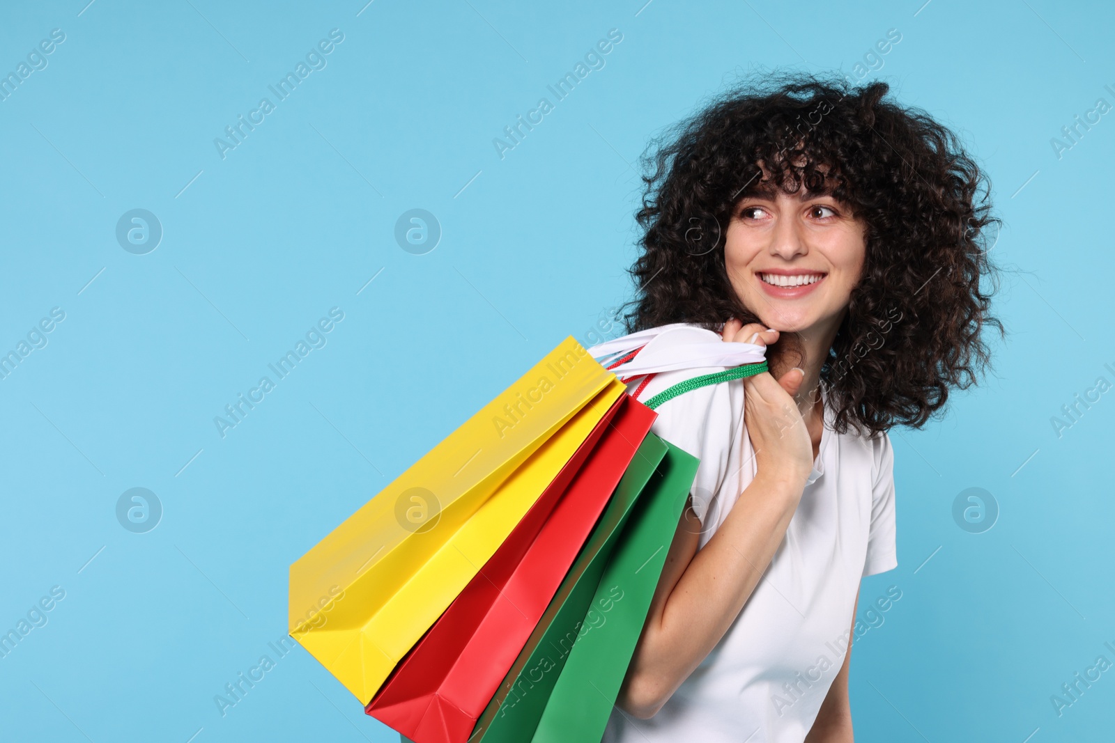 Photo of Happy young woman with shopping bags on light blue background. Space for text