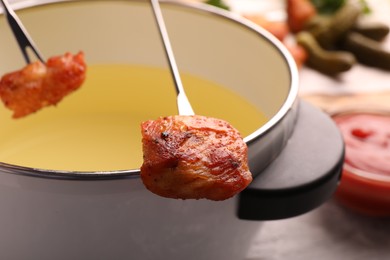 Photo of Fondue pot and forks with fried meat pieces on grey table, closeup