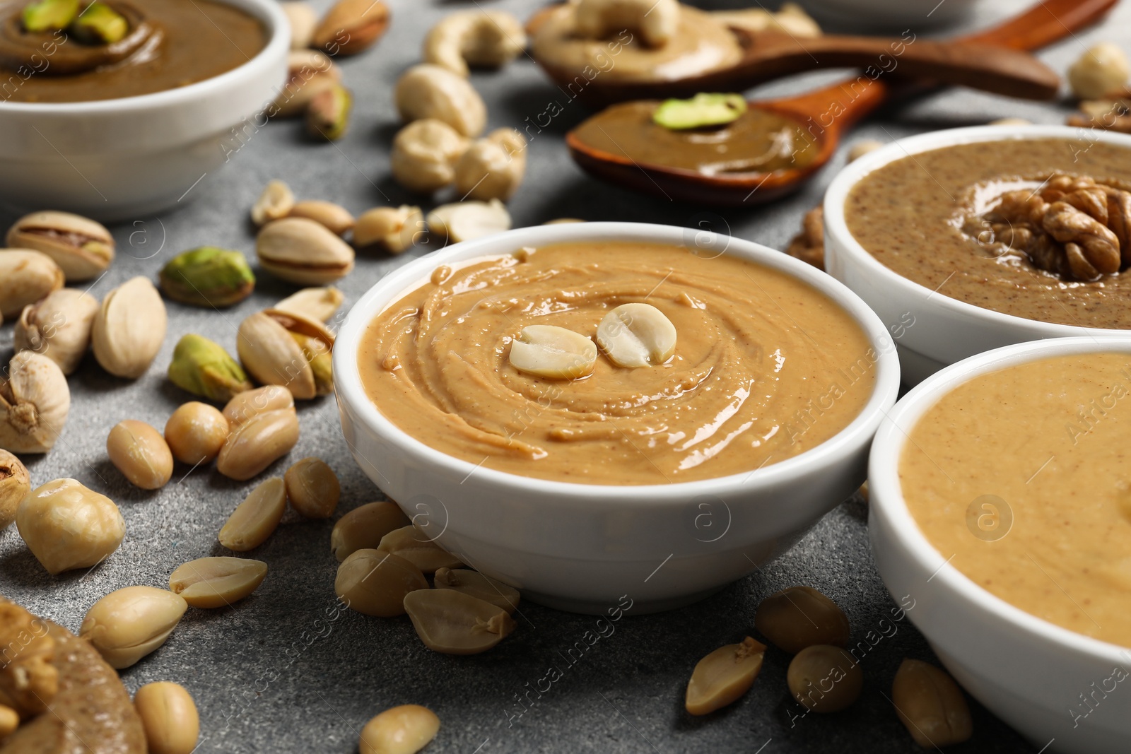 Photo of Tasty nut butters in bowls and raw nuts on light grey table, closeup