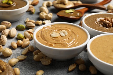 Photo of Tasty nut butters in bowls and raw nuts on light grey table, closeup