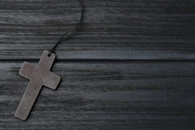 Photo of Christian cross on black wooden table, top view. Space for text