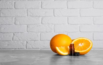 Photo of Bottle of essential oil with oranges on grey marble table against white brick wall. Space for text