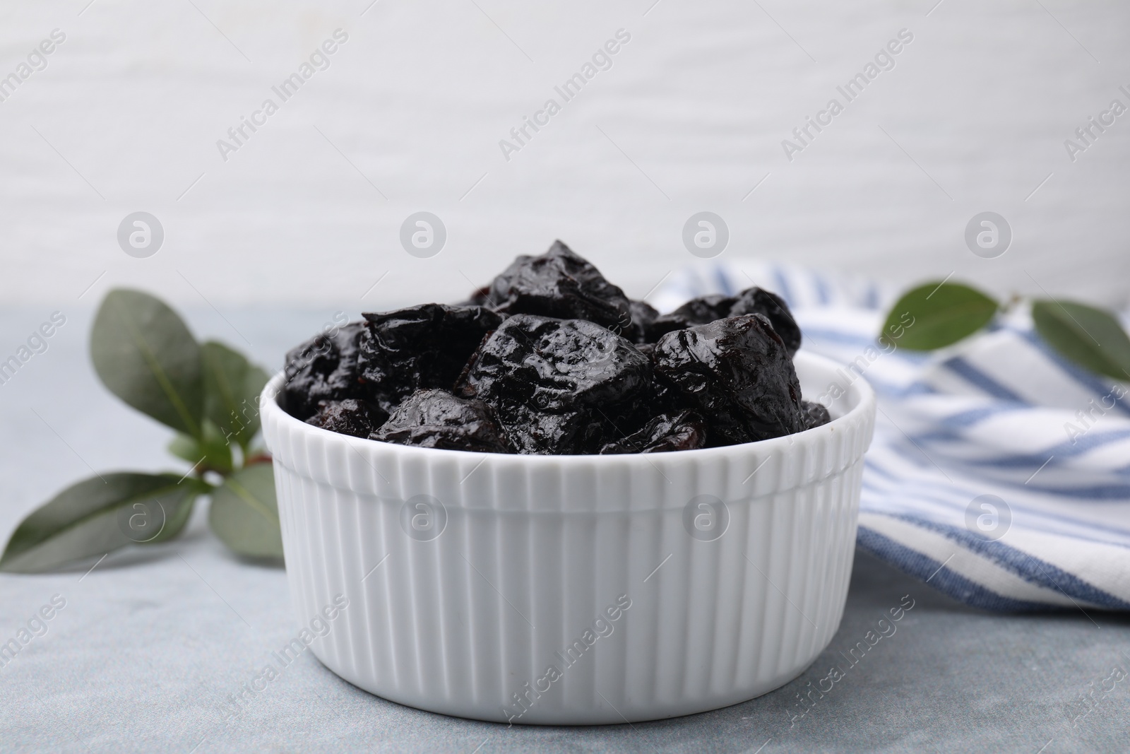 Photo of Sweet dried prunes in bowl on grey table, closeup