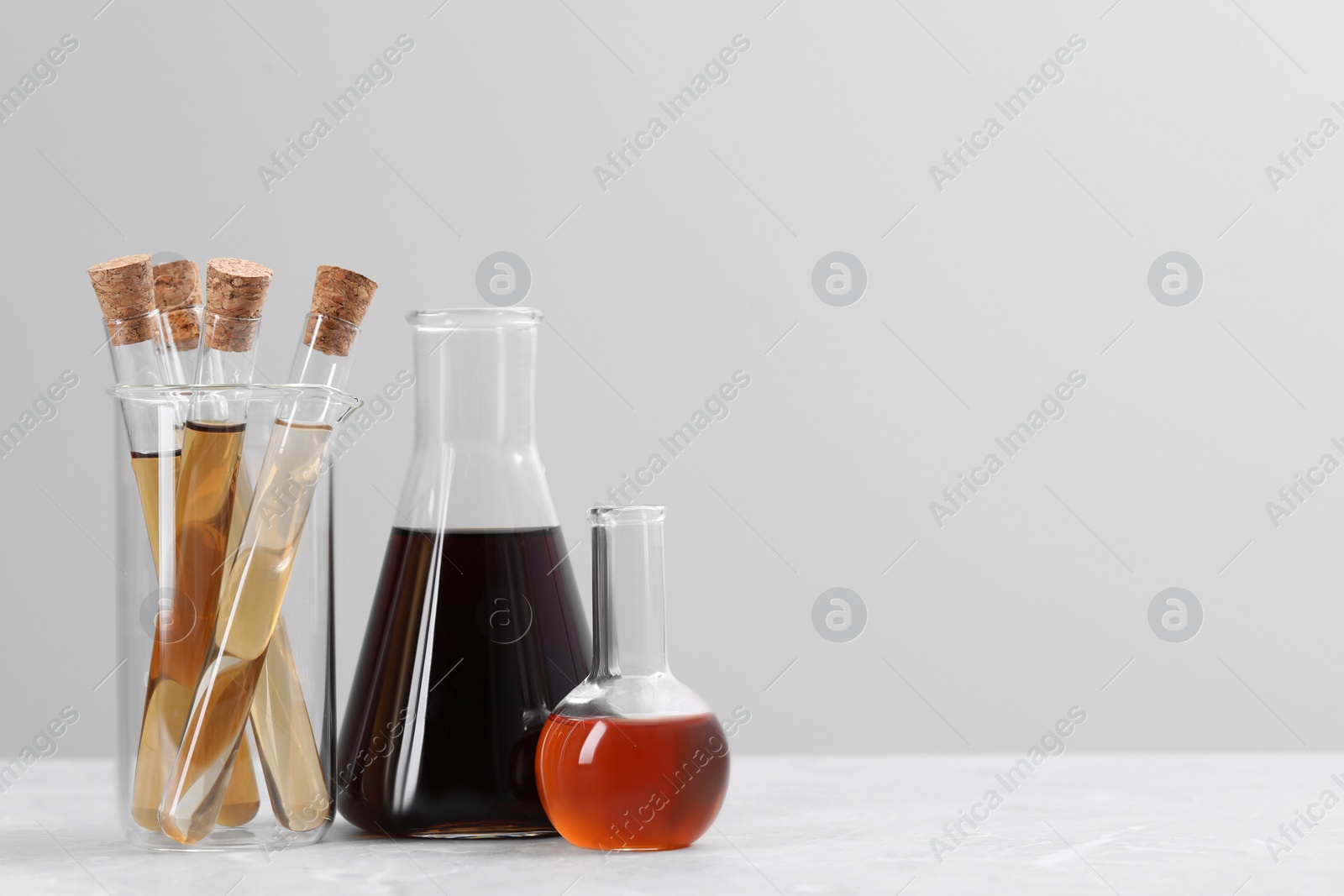 Photo of Different laboratory glassware with brown liquids on white table against light background. Space for text