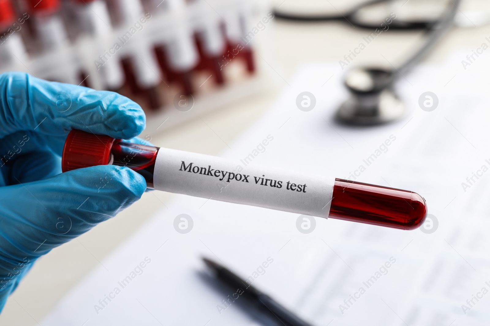 Photo of Laboratory worker holding test tube with blood sample over table, closeup