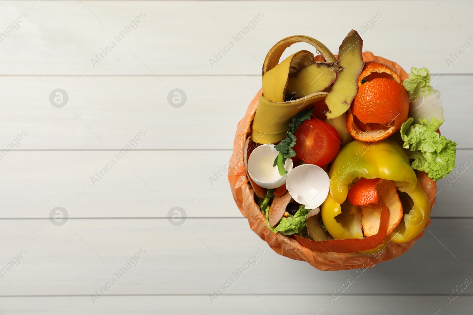 Photo of Natural garbage in trash bin on white wooden background, top view with space for text. Composting of organic waste