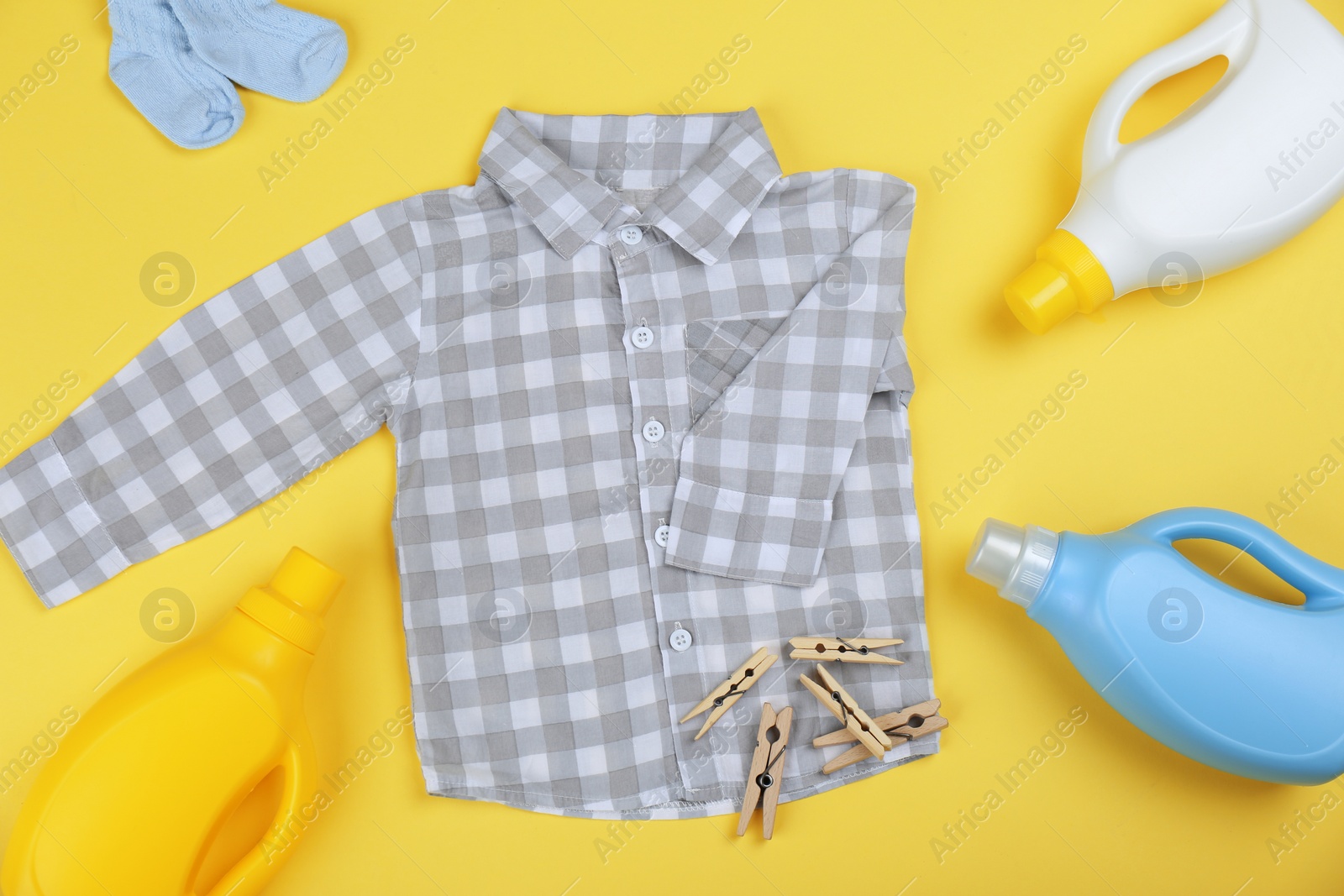 Photo of Flat lay composition with detergents and children's clothes on yellow background