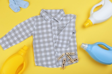 Photo of Flat lay composition with detergents and children's clothes on yellow background