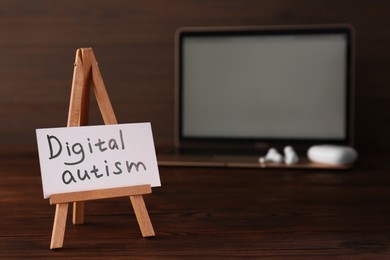 Photo of Card with phrase Digital Autism and laptop on wooden table, selective focus