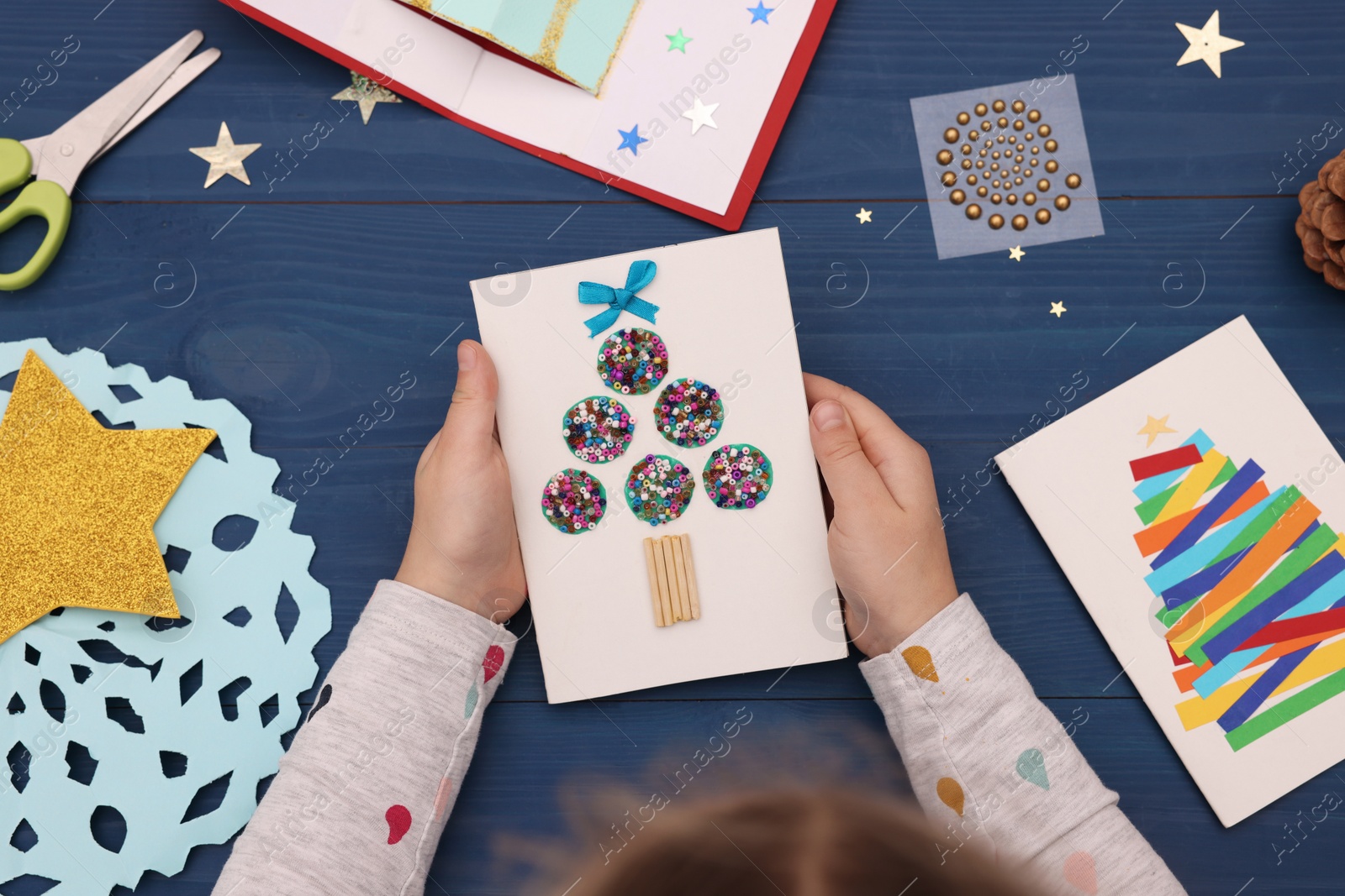 Photo of Little child with beautiful Christmas card at blue wooden table, top view