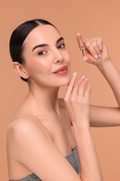 Beautiful young woman holding skincare ampoule on beige background