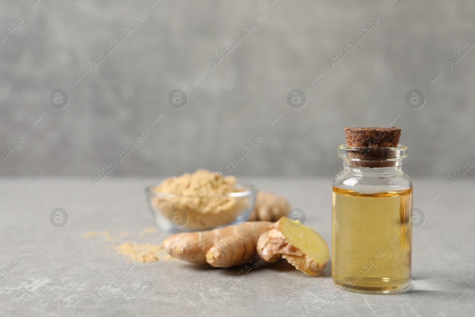 Photo of Glass bottle of essential oil and ginger root on grey table, space for text