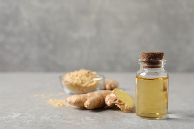 Glass bottle of essential oil and ginger root on grey table, space for text