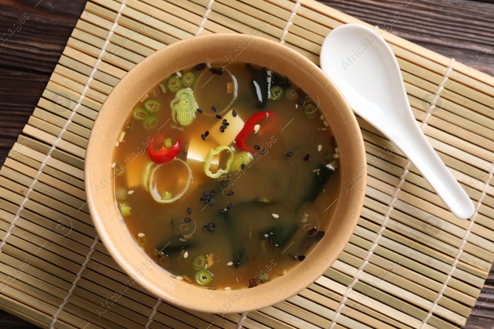Photo of Bowl of delicious miso soup with tofu and spoon on wooden table, top view