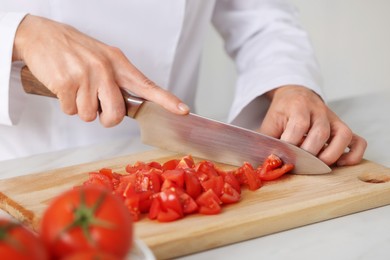 Photo of Professional chef cutting tomatoes at white marble table indoors, closeup