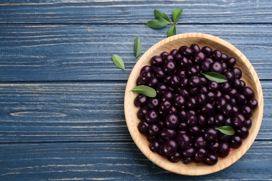 Photo of Fresh acai berries in bowl and leaves on blue wooden table, flat lay. Space for text