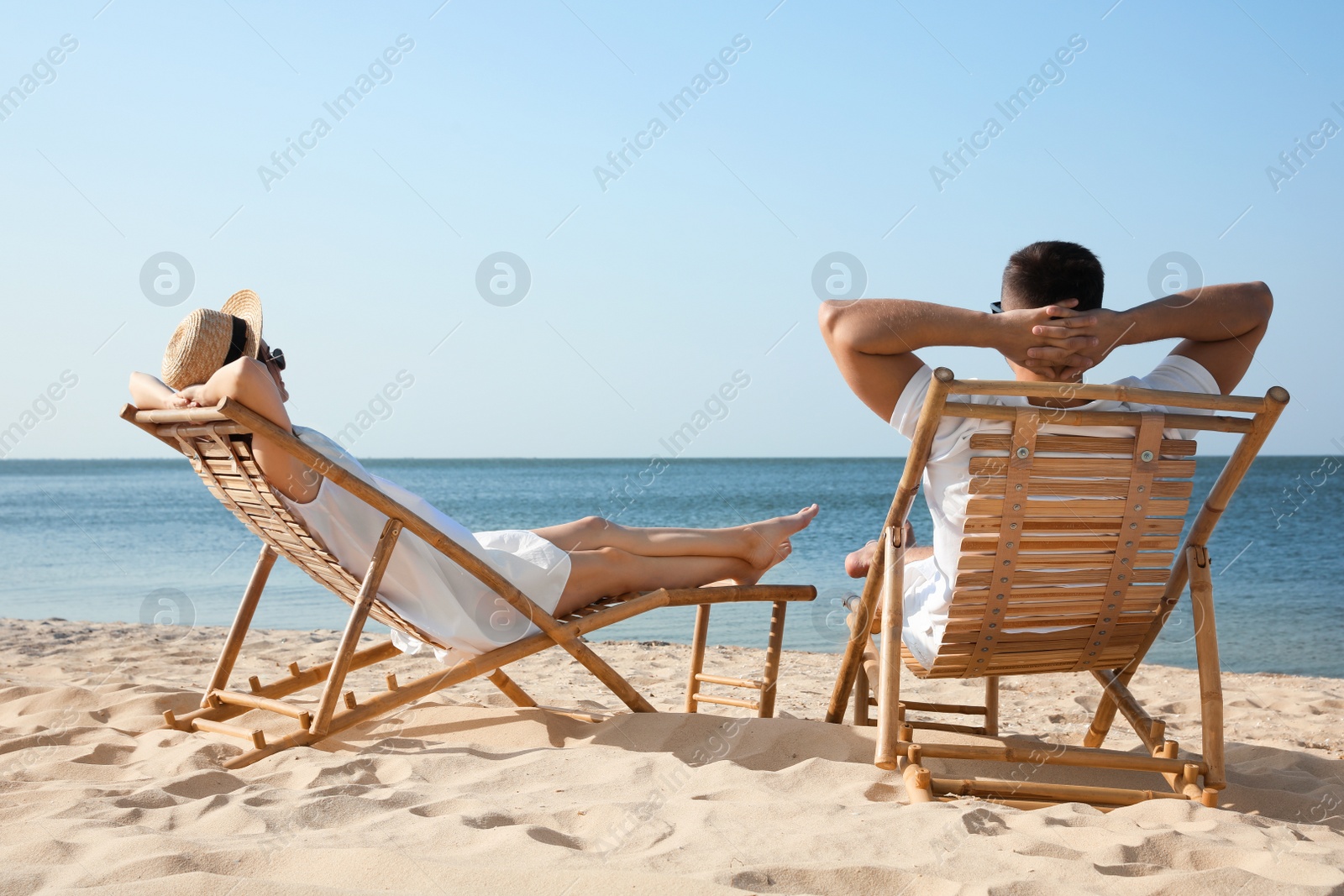 Photo of Young couple relaxing in deck chairs on beach