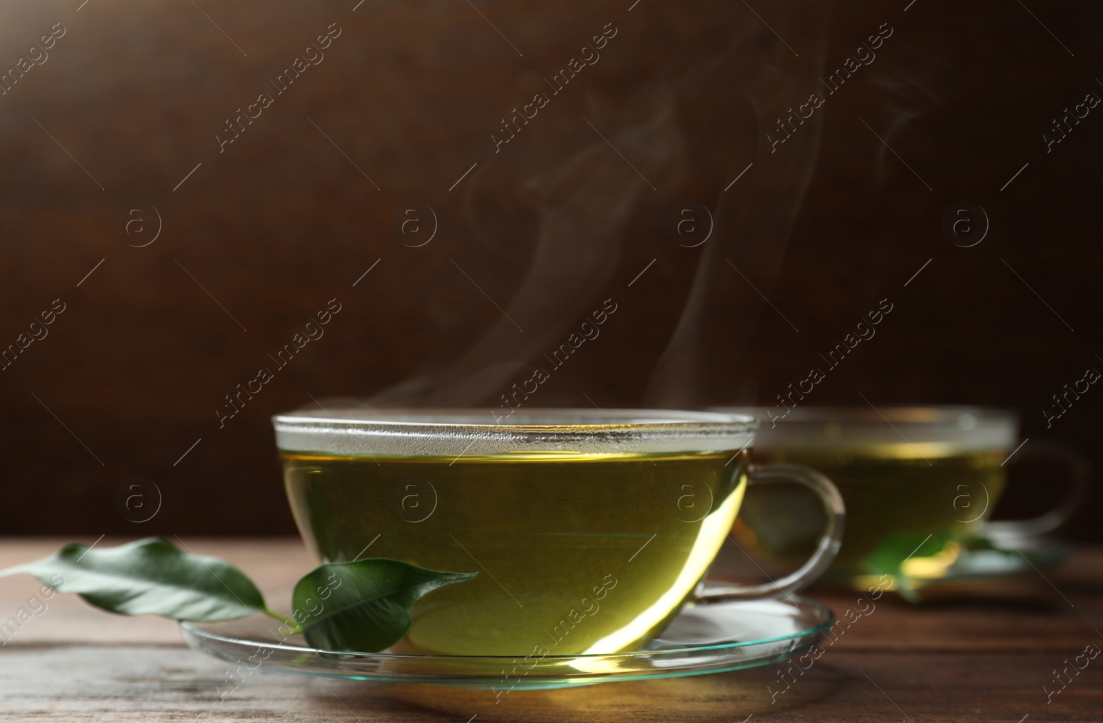 Photo of Fresh green tea in glass cup with saucer and leaves on wooden table