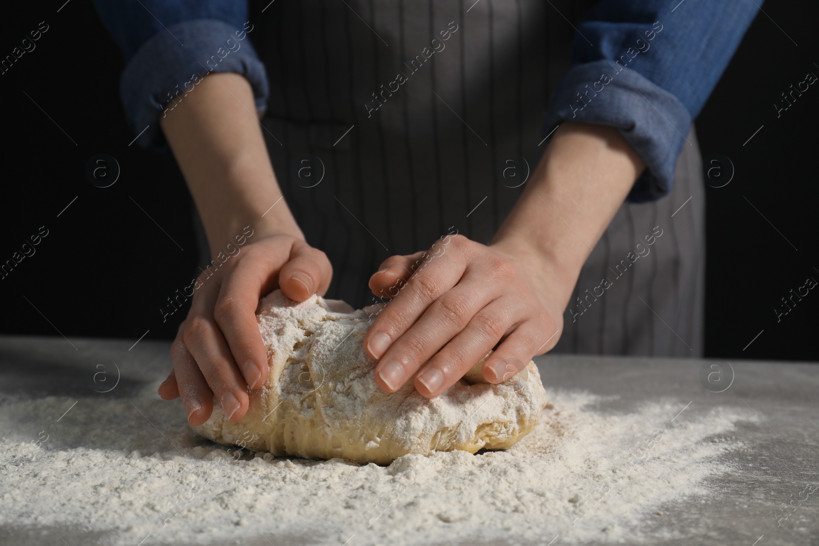 Photo of Making bread. Woman kneading dough at table on dark background, closeup