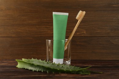 Photo of Aloe vera toothpaste in blank tube, brush and green leaves on wooden table, space for text