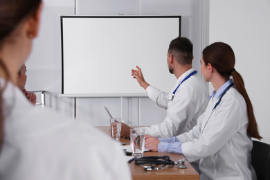 Photo of Team of doctors looking at projection screen indoors. 
Video conference