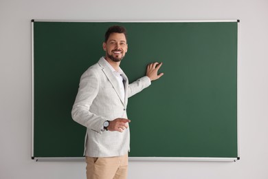 Photo of Happy teacher explaining something at blackboard in classroom. Space for text