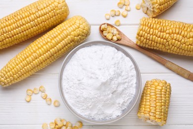 Photo of Bowl with corn starch, ripe cobs and kernels on white wooden table, flat lay