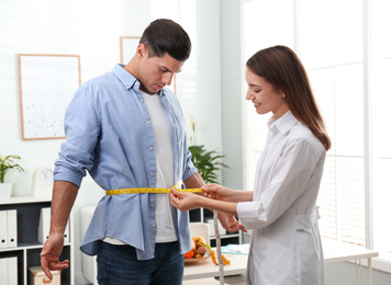 Photo of Young nutritionist measuring patient's waist in clinic